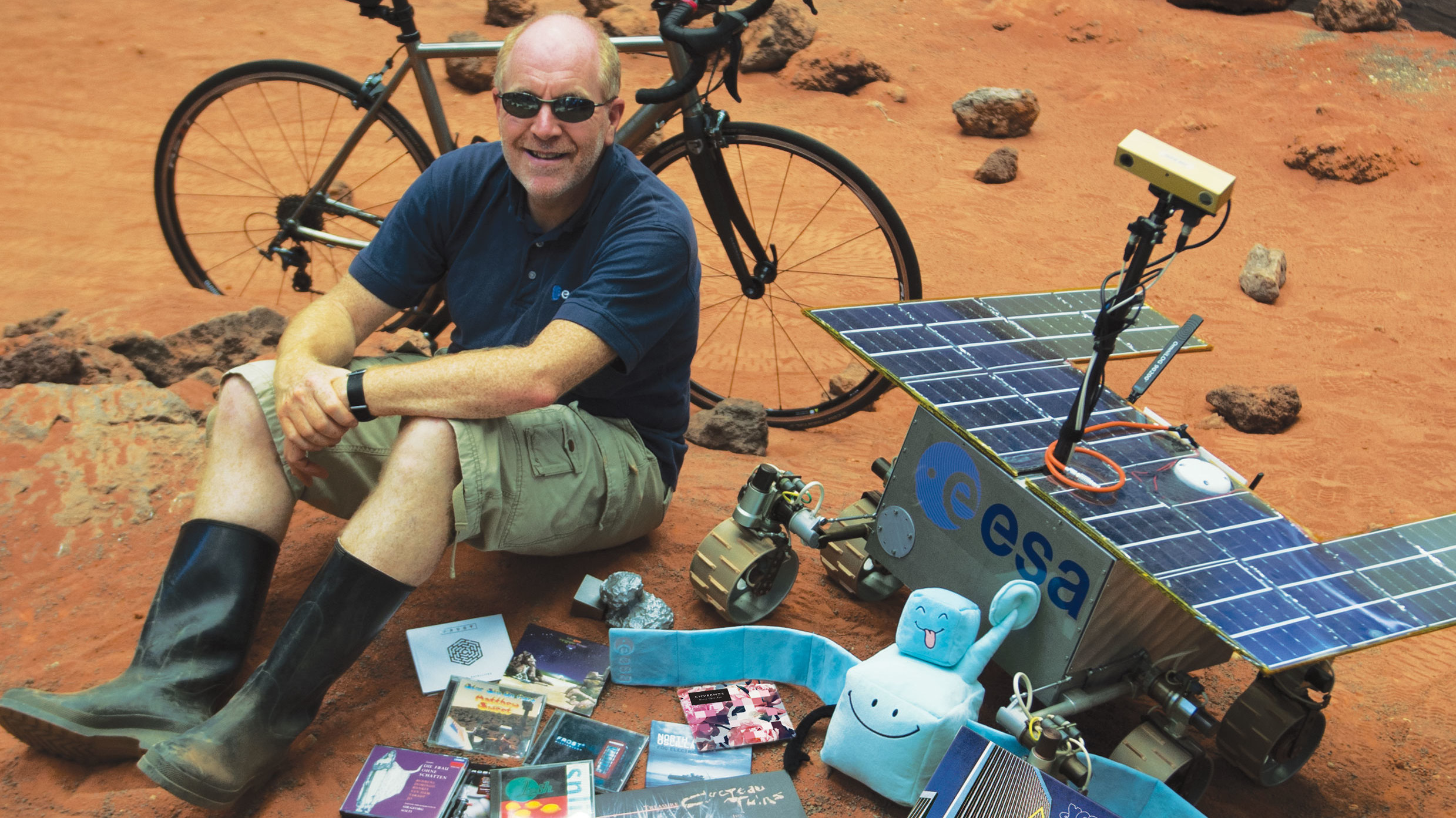 Mark McCaughrean sitting on an orange hill surrounded by records and space agency items