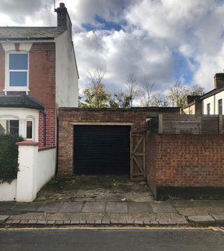 An old garage with black door connected to a house and brick wall on either side