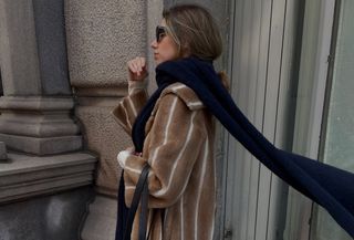 Robin wears a brown and fur fur coat, navy scarf, and black bag.