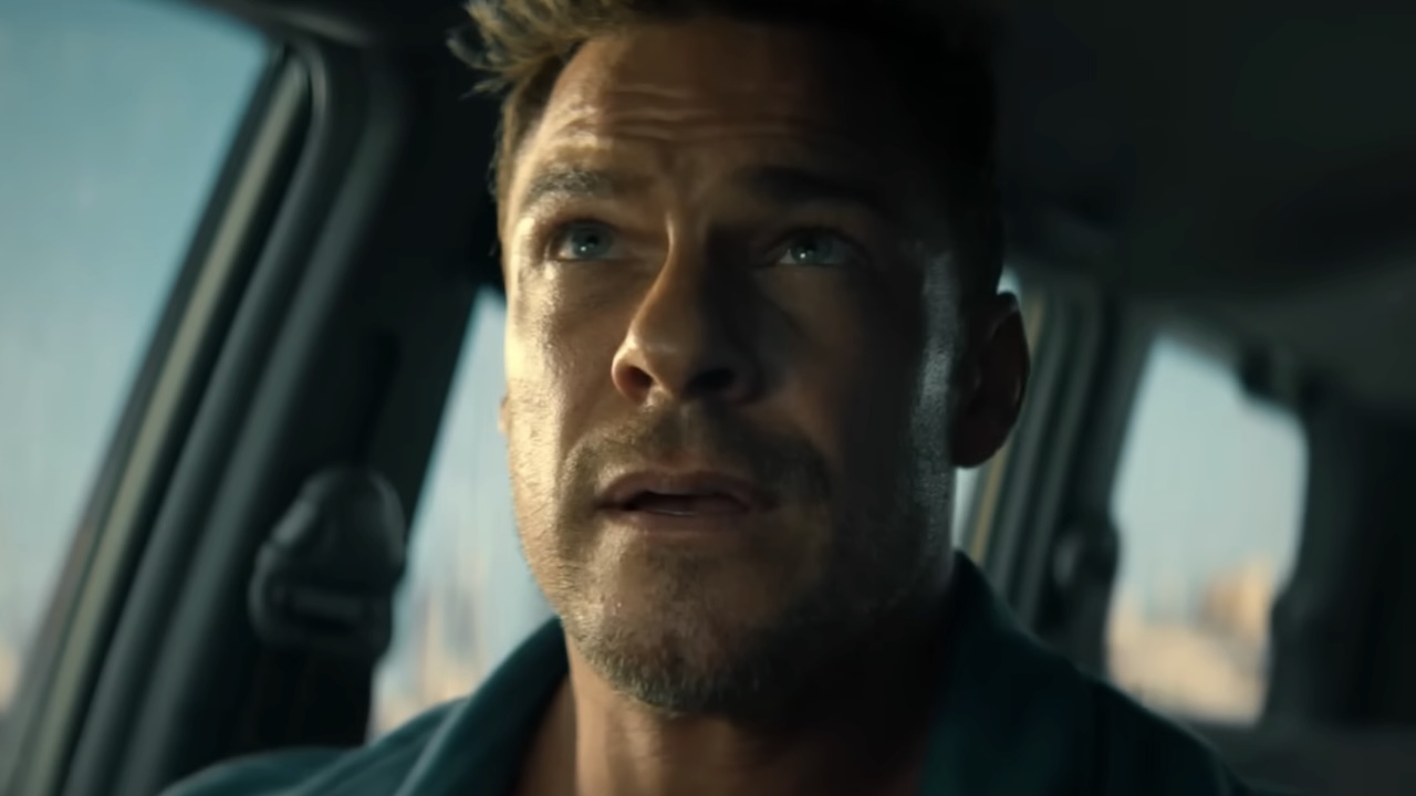 Alan Ritchson sitting in car passenger seat looking up in Runner