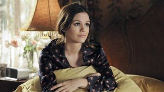 Rachel Bilson sits on a bed holding a cushions in Hart of Dixie