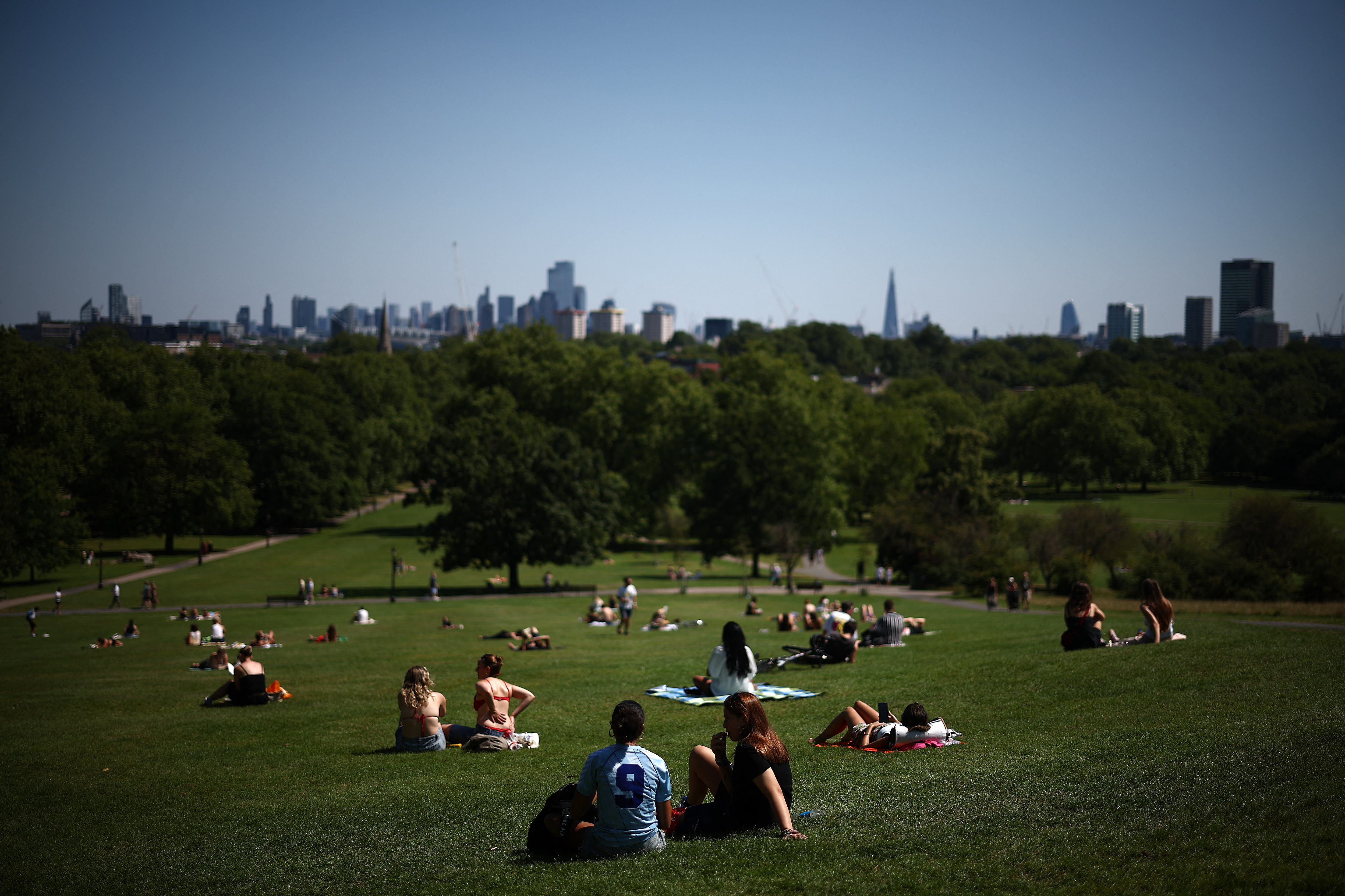 People enjoy the hot weather, sitting in the sun, backdropped by the skyline of central London, from Primrose Hill on July 29, 2024.