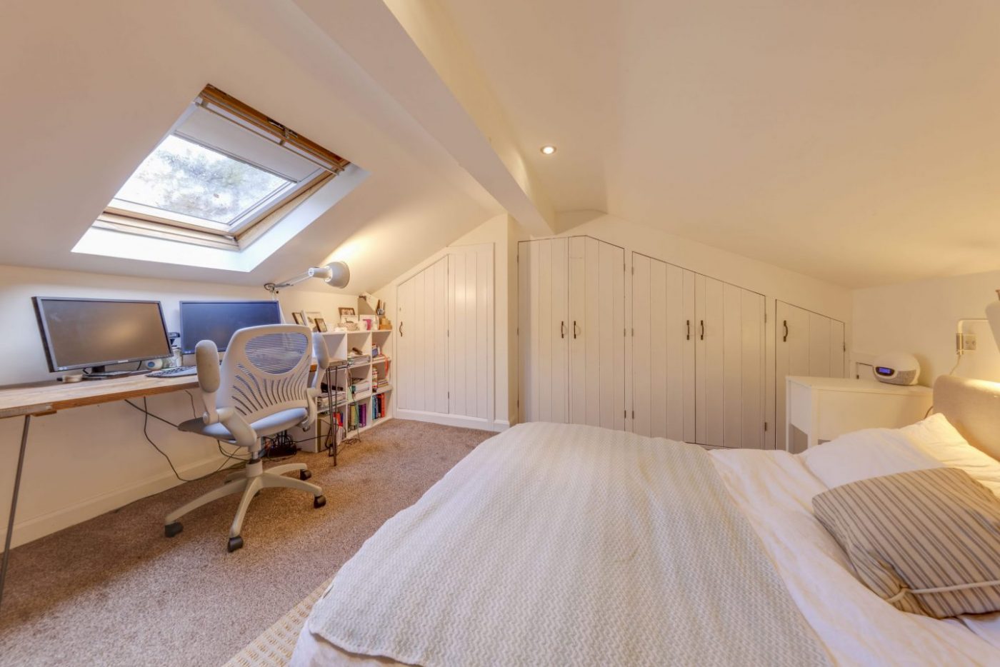 Master bedroom with white decor and a home working setup beneath a skylight