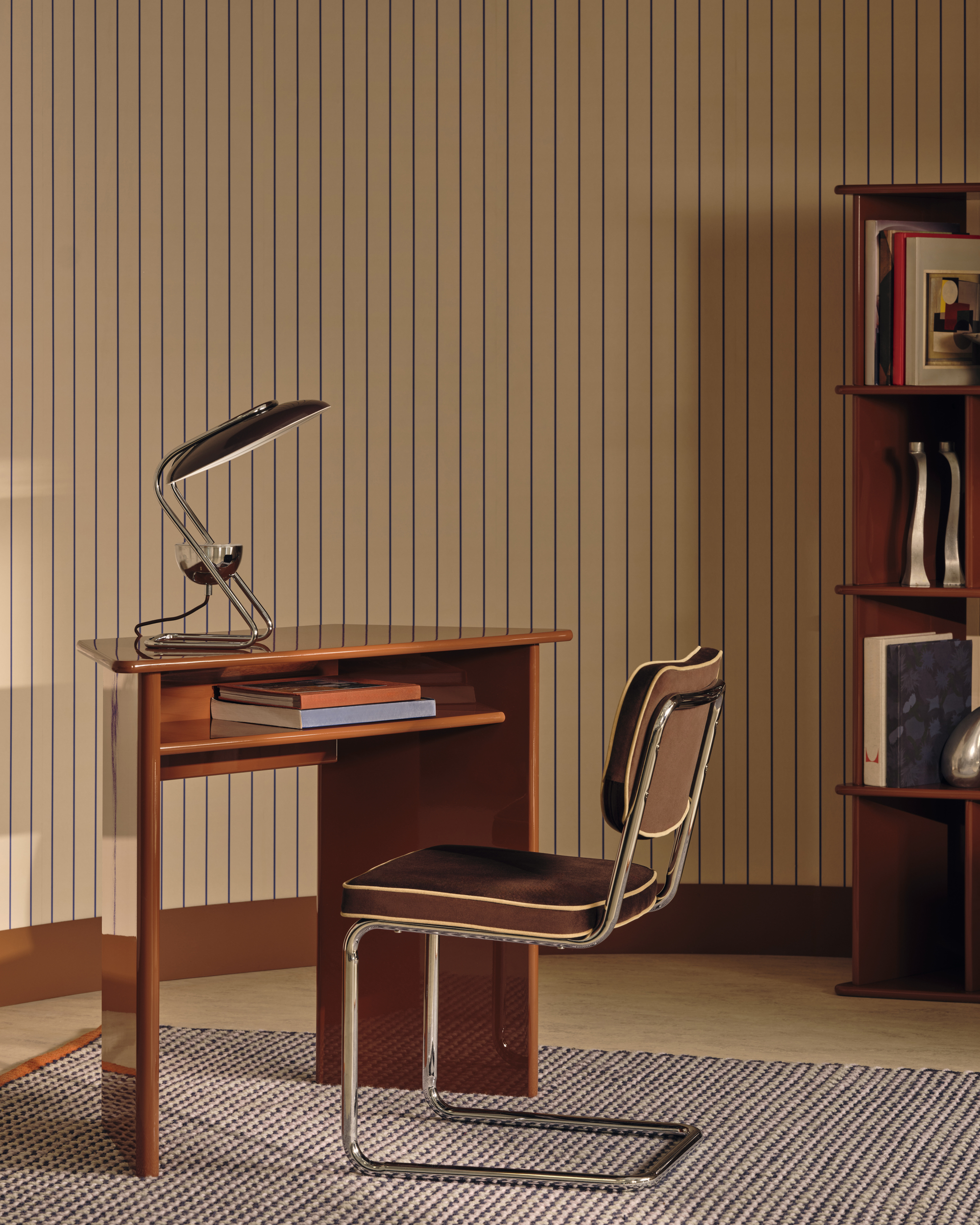 Image of a colorful, mid-century modern style room with a small orange lacquer desk with a brown and metal desk chair. The walls have a cream and navy pinstripe design.