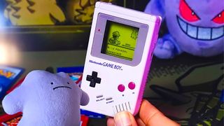 Photo of hand holding Game Boy Jukebox next to sad Ditto plush.