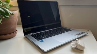 A Chromebook is open on a desk next to a pair of AirPods Pro 2