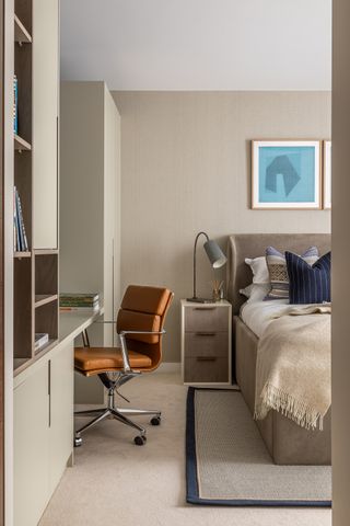 neutral bedroom with home office, carpet, textured wallpaper, fitted units and desk, leather chair, side table, lamp, artwork