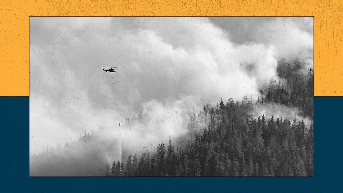 A helocopter drops water over a burning forest.