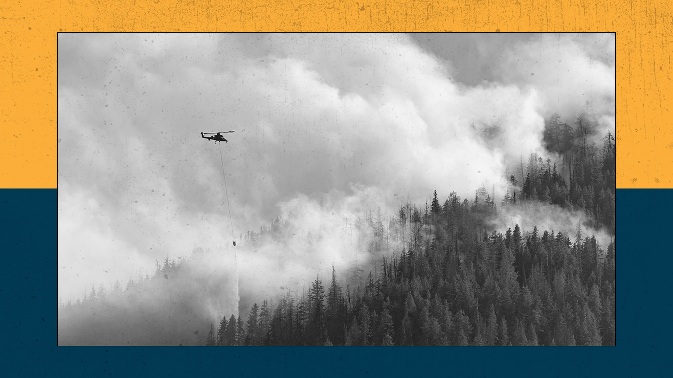 A helocopter drops water over a burning forest.