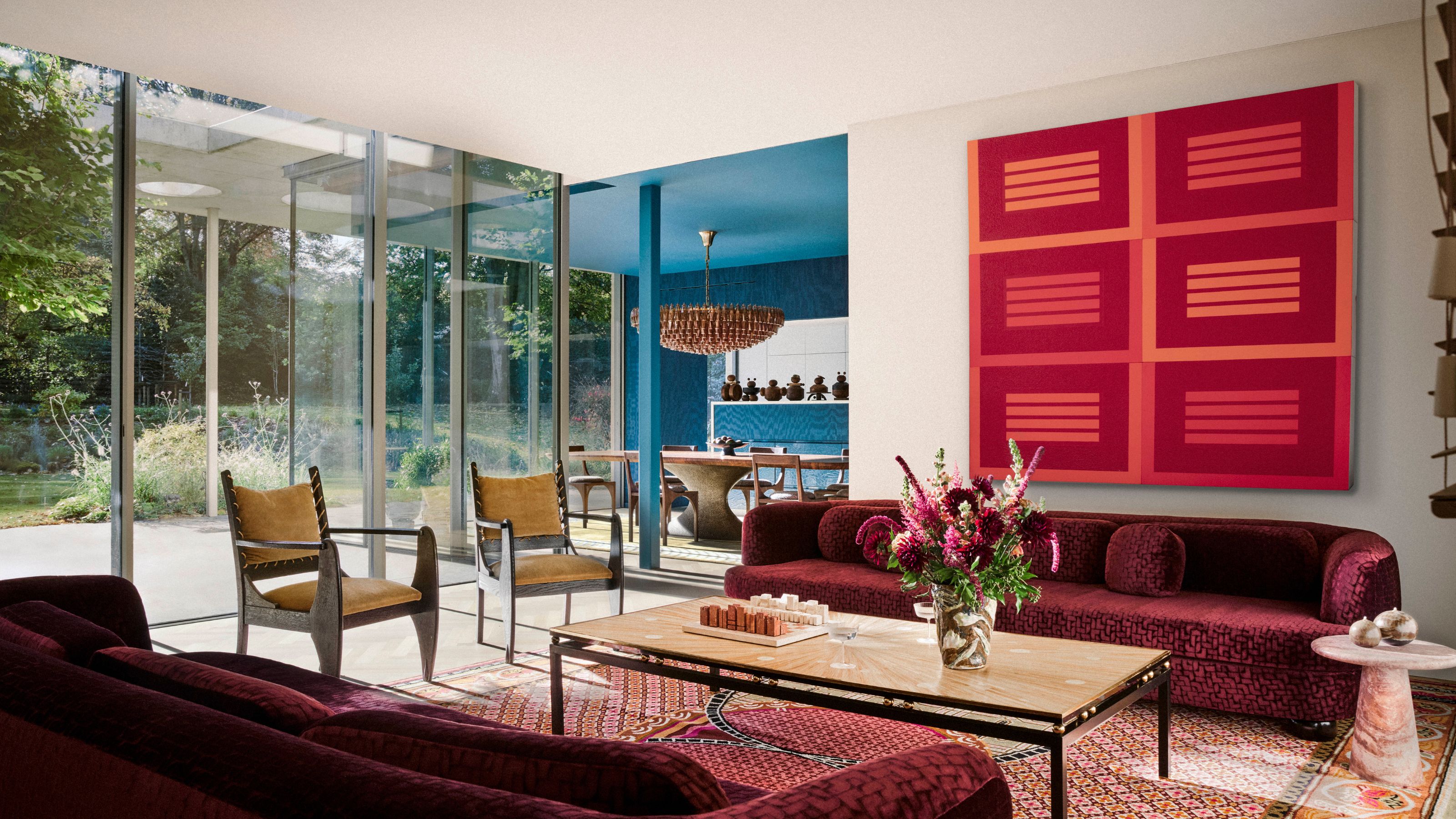 A living room with deep red sofa, a red artwork and tall windows opening up to the garden