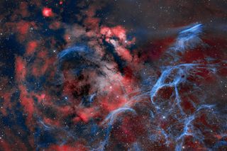 The vela supernova remnant is a rich tapestry of billowing red and blue clouds of gas with stars speckled throughout. An elongated glowing blue nebula fills the top left portion of the image, this is the Pencil Nebula.