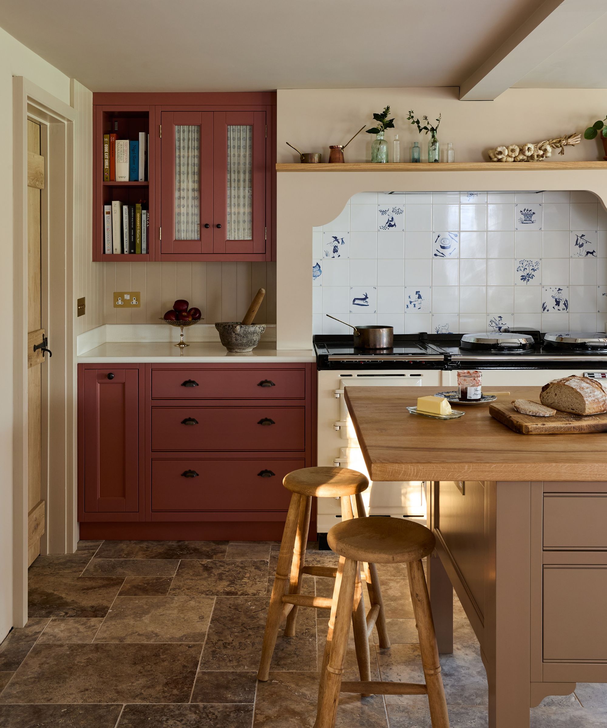A country kitchen with rusty red cabinets, a wooden island, and a mixed material backsplash
