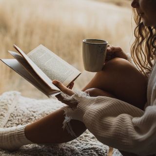 A young woman enjoying a book while drinking a hot beverage.