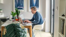 Side view of a man on his laptop, working from home at his dining table