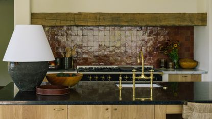 a contemporary meets rustic kitchen with oak cabinetry, rustic beams, and oxblood red zellige tile backsplash behind the range cooker 