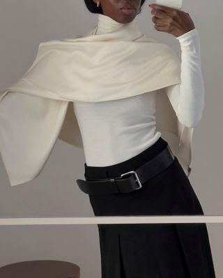 Sylvie Mus wearing a cream silk cape with a cream turtleneck sweater and belted skirt.