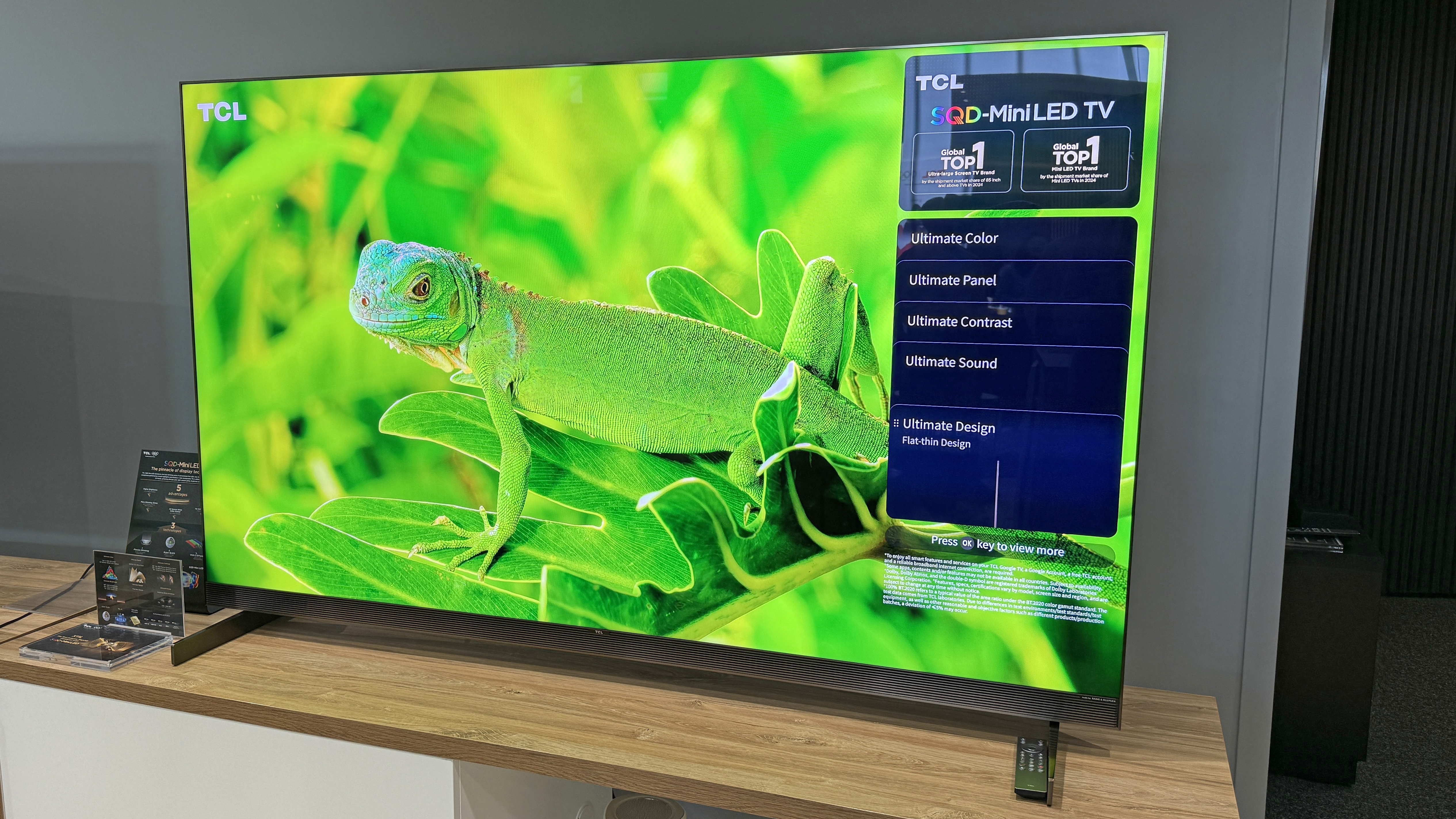 The TCL X11L TV at a launch event, showing an image of vibrant green lizard against very lush green vegetation