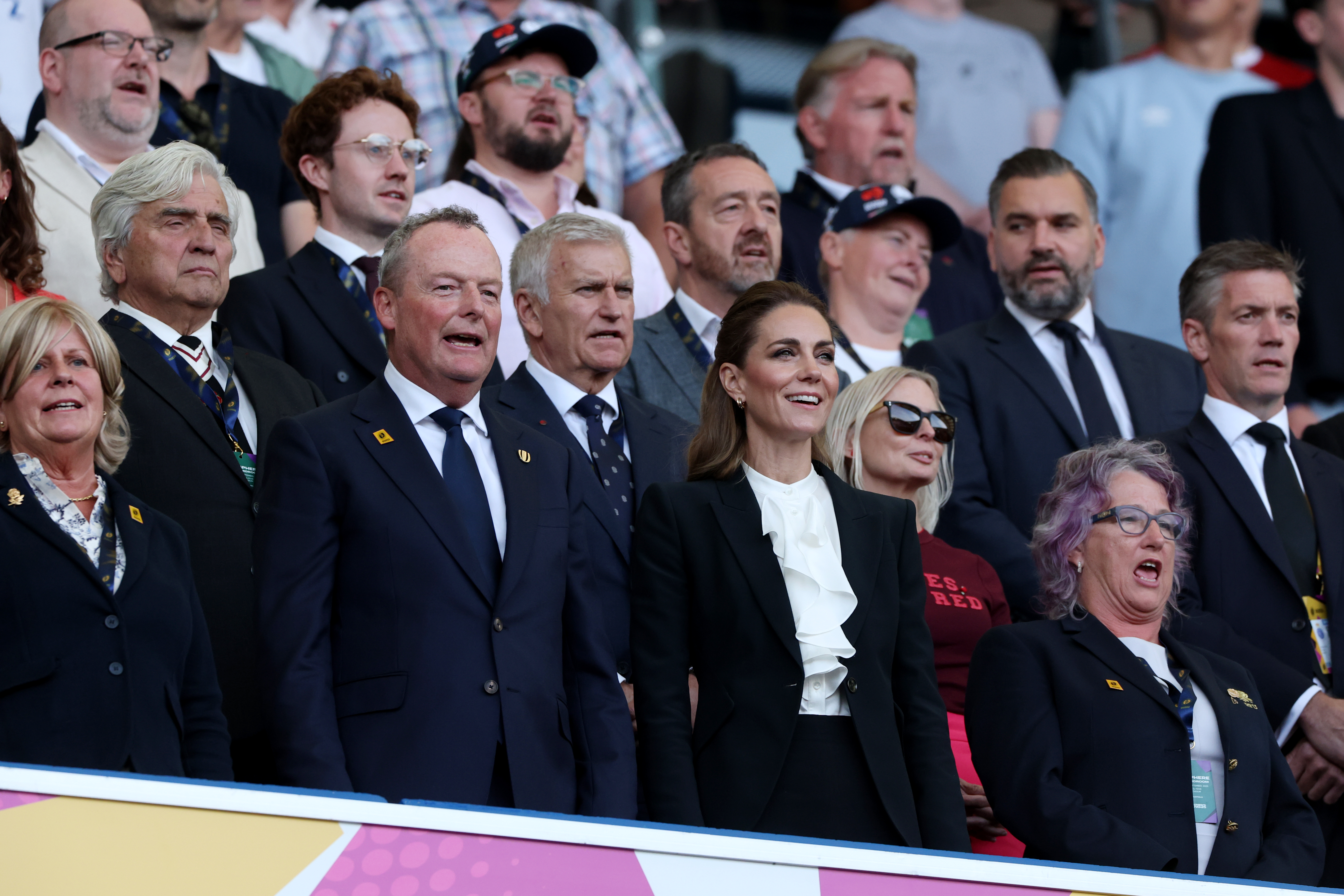 Kate Middleton in a black suit and white ruffled shirt