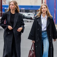 Twins Amalie & Cecilie Moosgaard wearing black trench coat, denim jeans, white button shirt outside Ulla Johnson on February 11, 2024 in New York City.