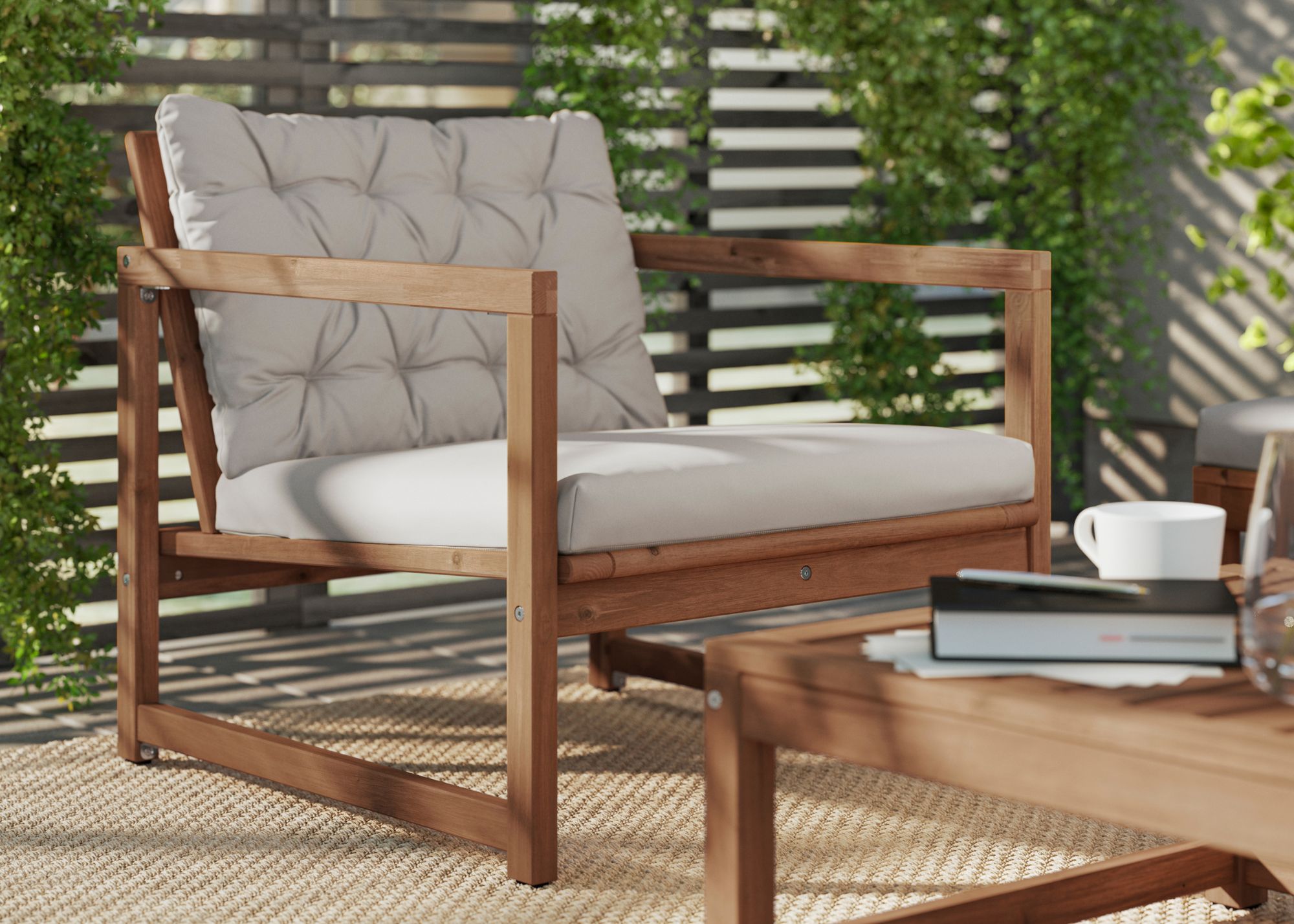 IKEA'S Naemarroe outdoor lounge chair in front of a coffee table with a book and coffee cup in front of a wood slatted fence with climbing foliage across sections of it