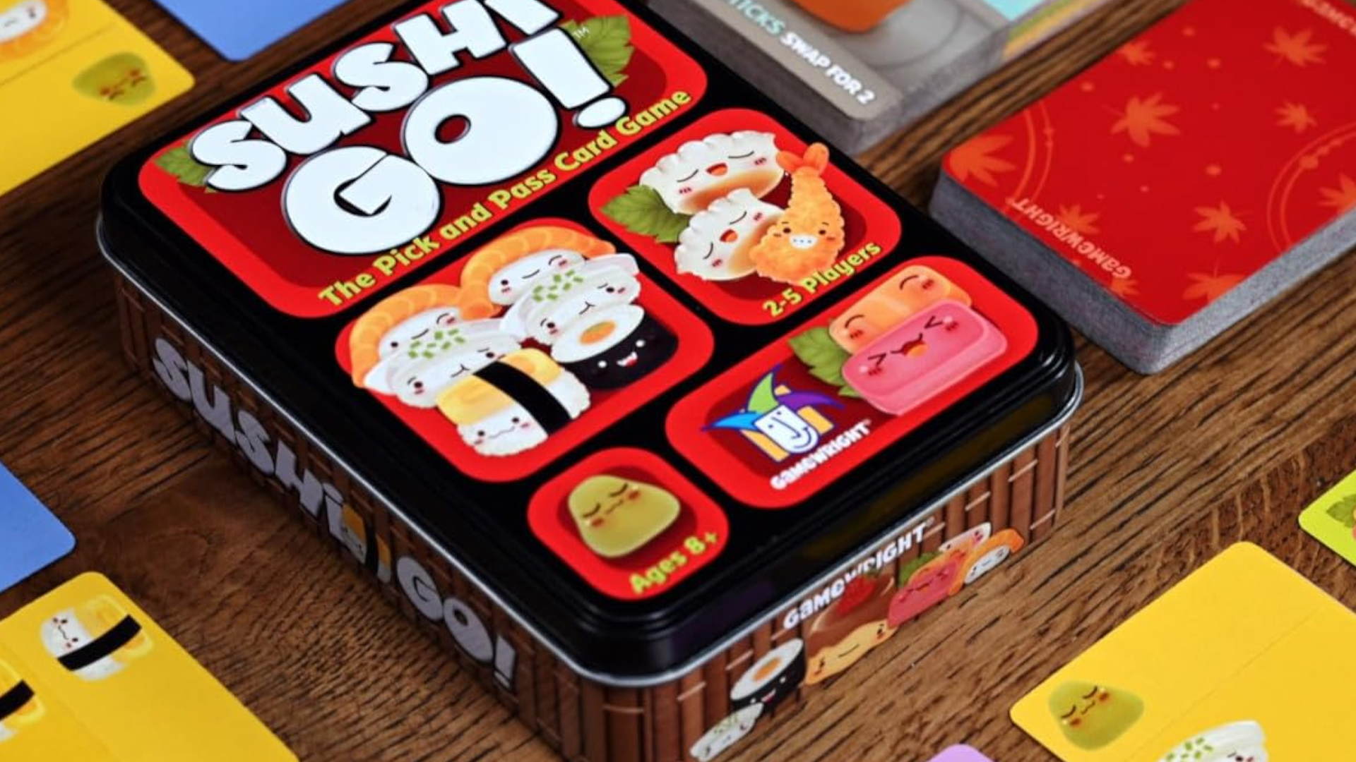 A Sushi Go box alongside a selection of cards on a wooden surface