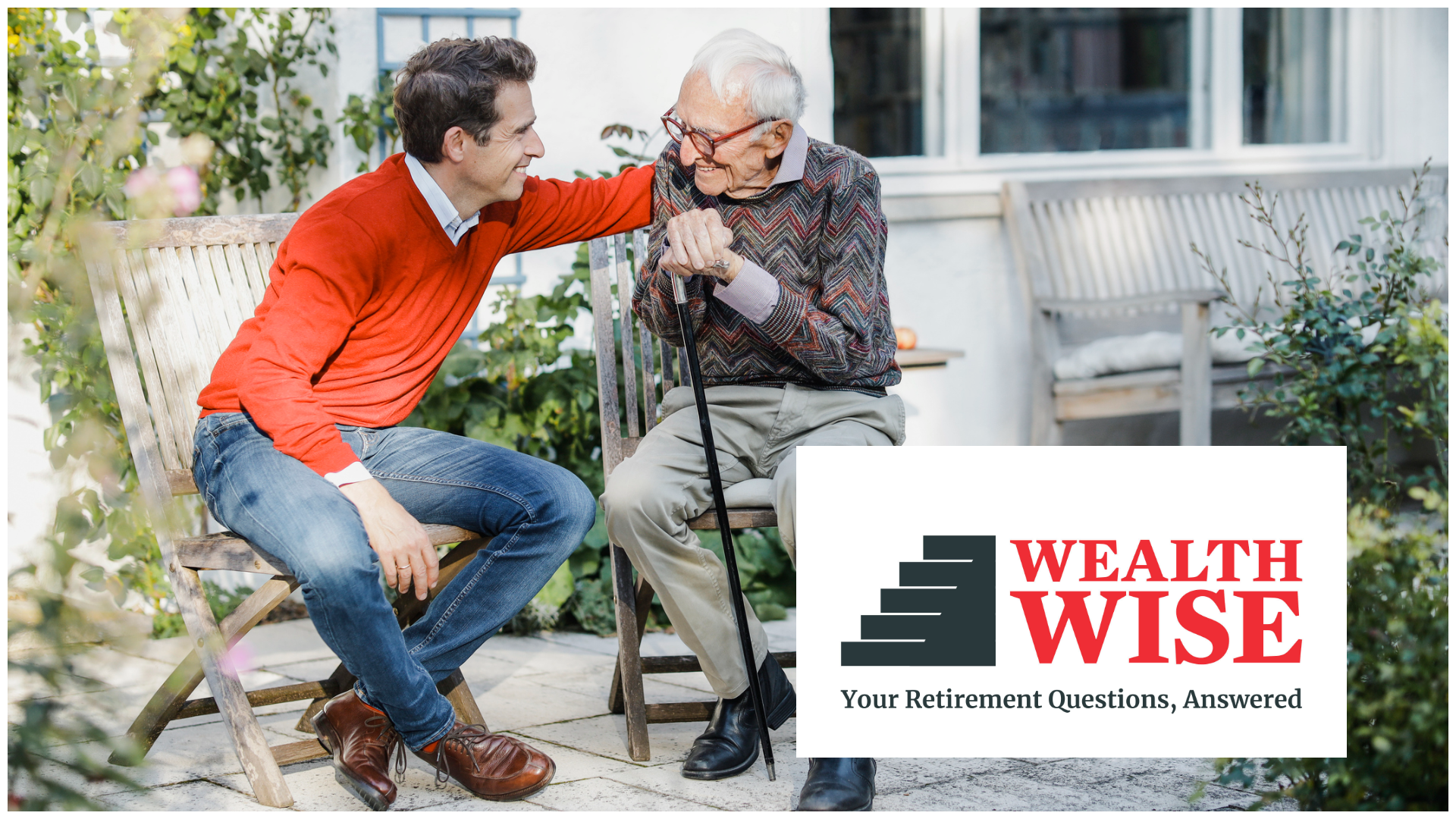 A man puts his elderly father on the back. His father is hunched over and holds a cane, but is smiling.