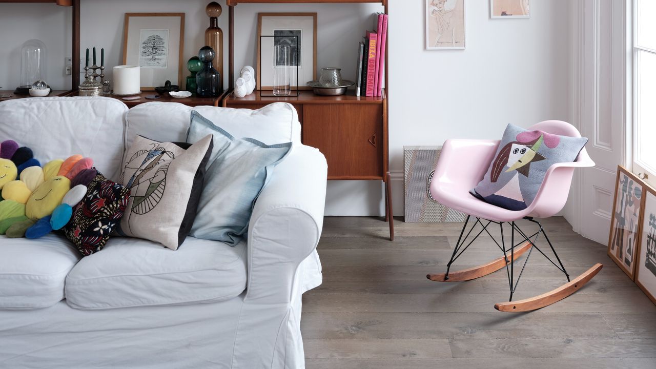 A living room with a light grey sofa at front with colourful cushions and a pink rocking chair to the side