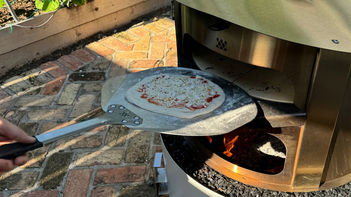 putting cheese pizza into the Breeo Live Fire pizza oven