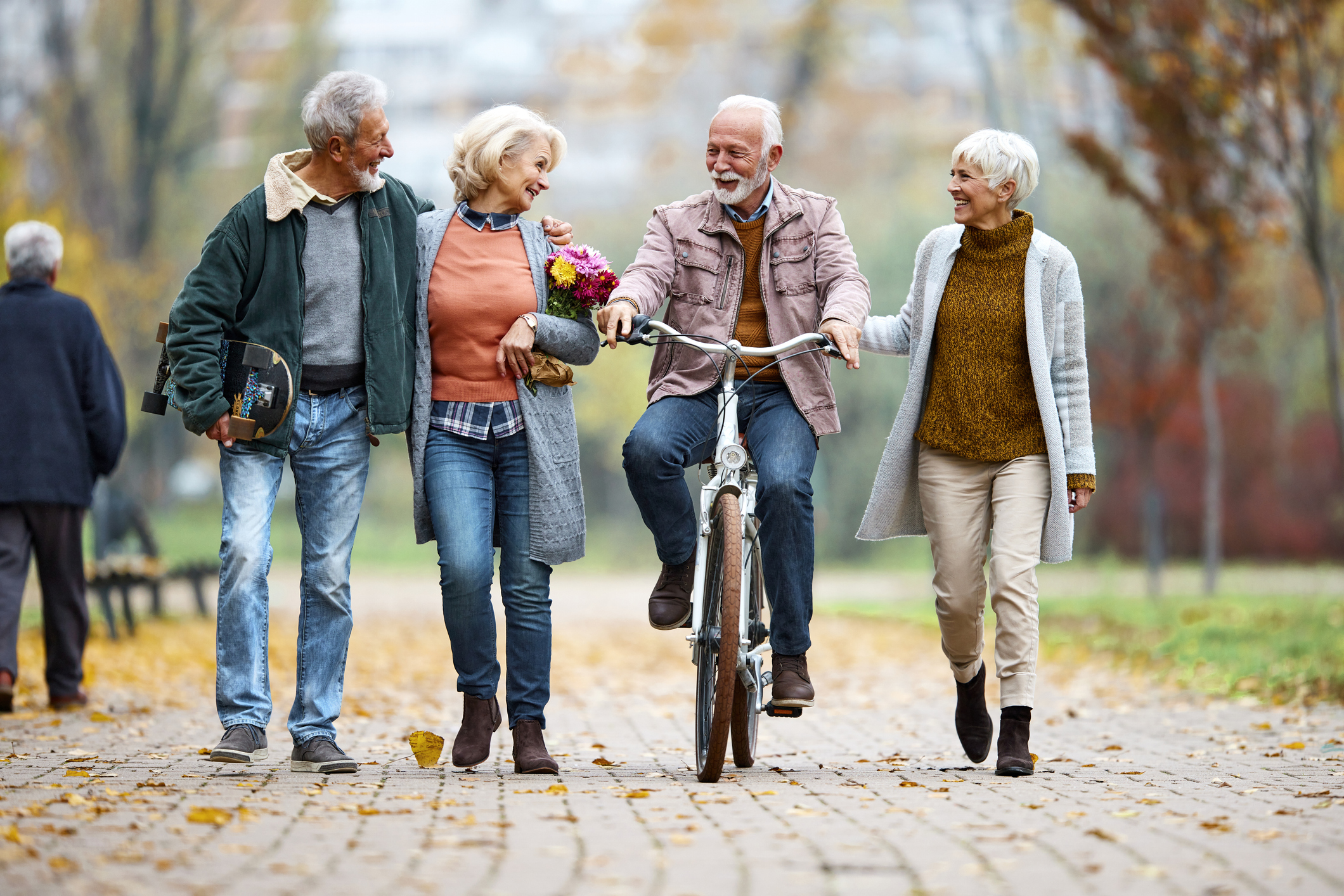 Happy senior couples enjoying while walking in autumn day at the park. Senior man is on a bike. Copy space.