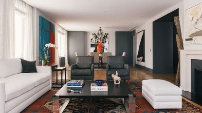 living room with white sofa and ottoman with bright patterned rug view to dining table and chandelier beyond