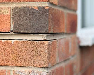 Gaps in red bricks on the corner exterior of a home with white window sill in soft focus in the background