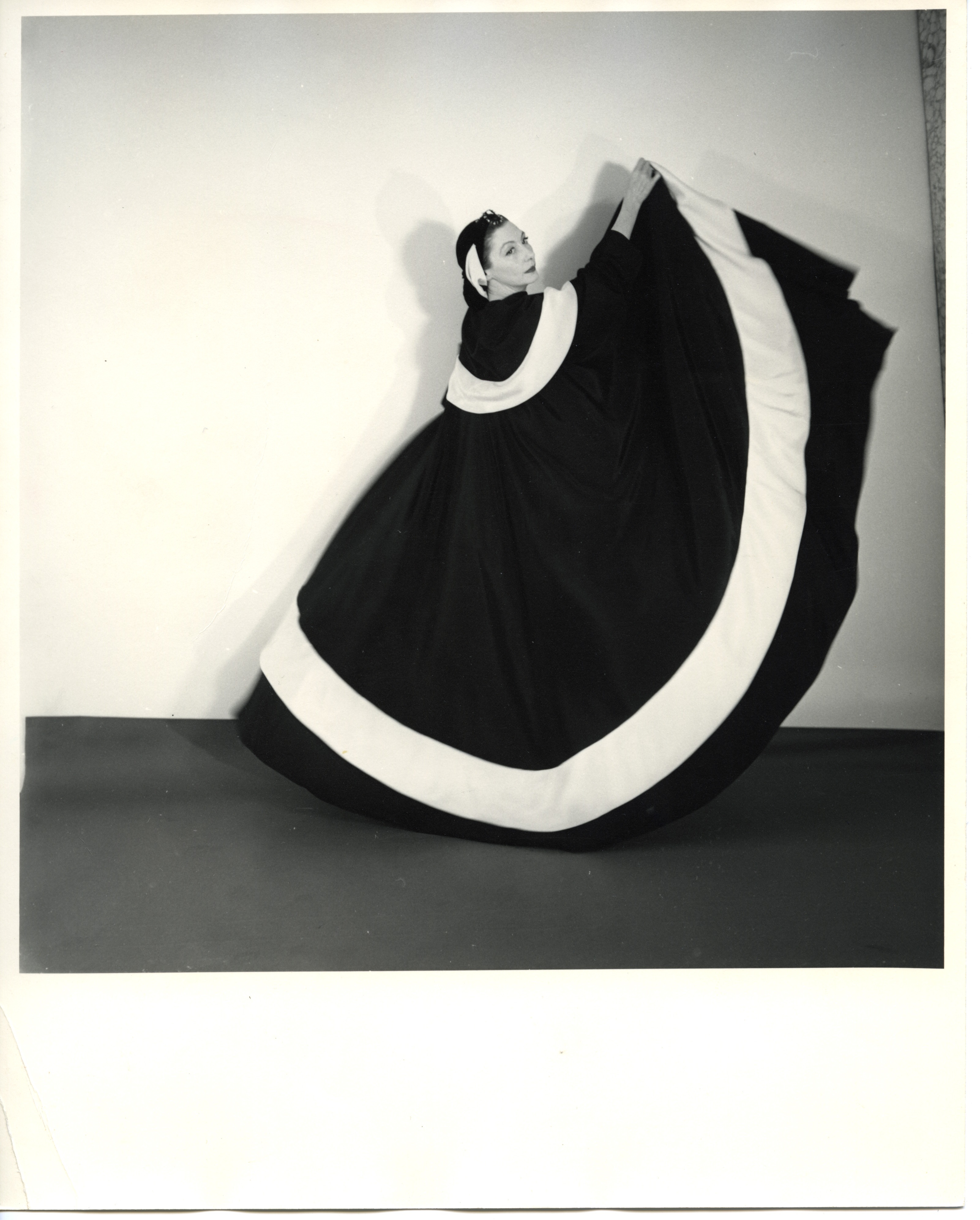 A woman in a dark gown with a bold white circular band holds the fabric aloft, creating a large, dramatic graphic shape against a plain wall.