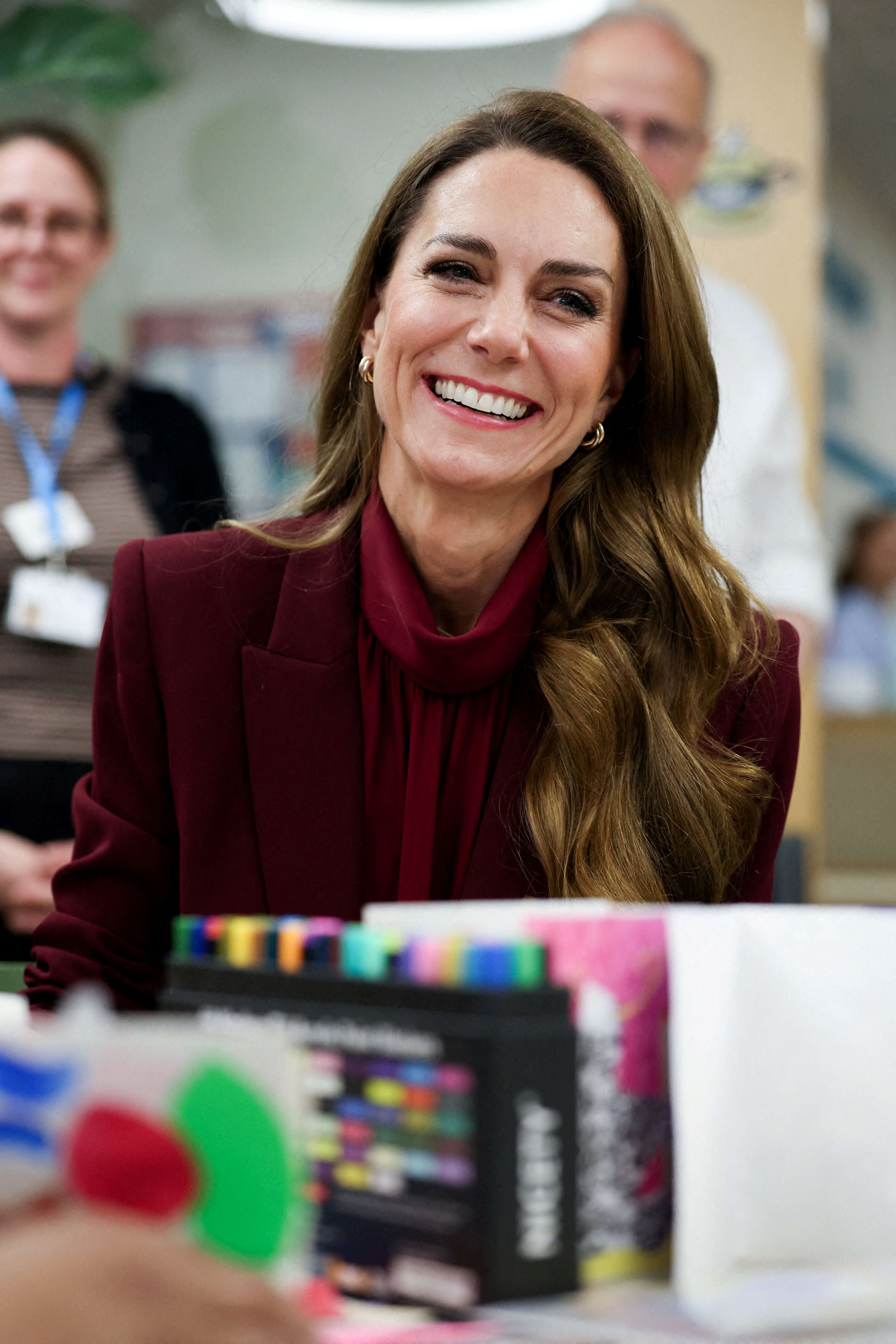 Princess Kate smiling wearing a burgundy suit jacket and top