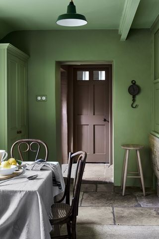 Painted green country kitchen, stone flooring, wooden dining table, looking out onto hallway with brown painted front door