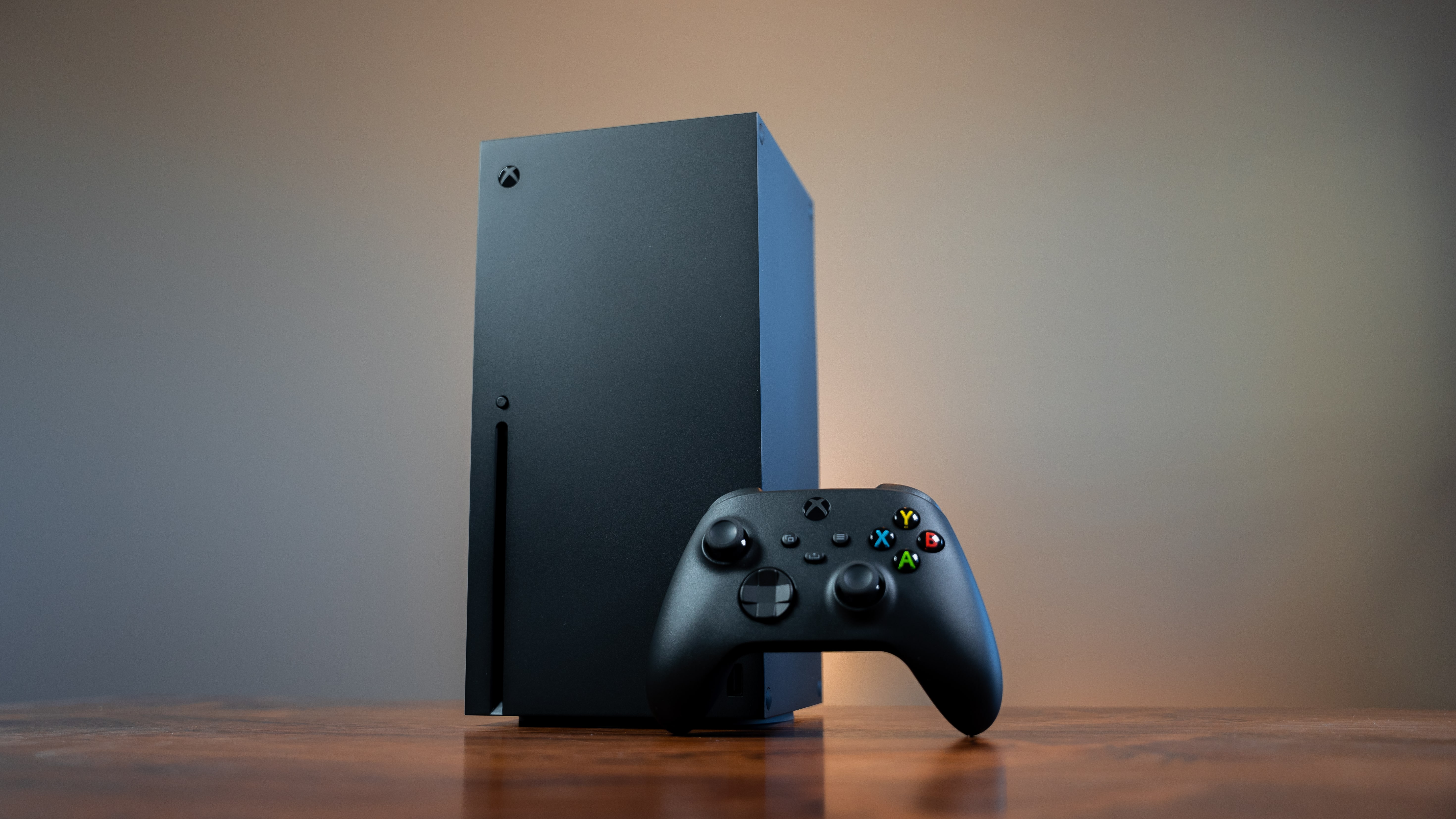 Looking up slightly at an Xbox Series X console with a controller leaning against the front.