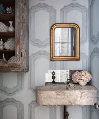 Powder room with grey Cole & Son wallpaper, stone sink and ornate mirror