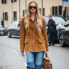 a blonde woman wears a suede jacket and jeans during fashion week
