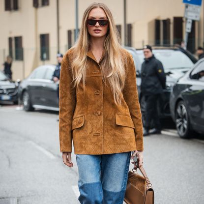 a blonde woman wears a suede jacket and jeans during fashion week