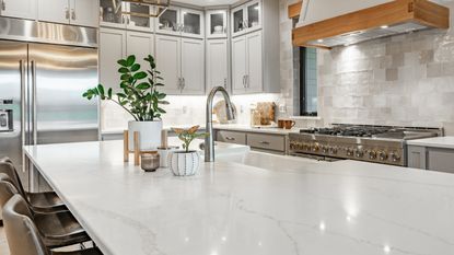 Natural white stone kitchen island within beautiful kitchen, with statement silver faucet by in-built sink