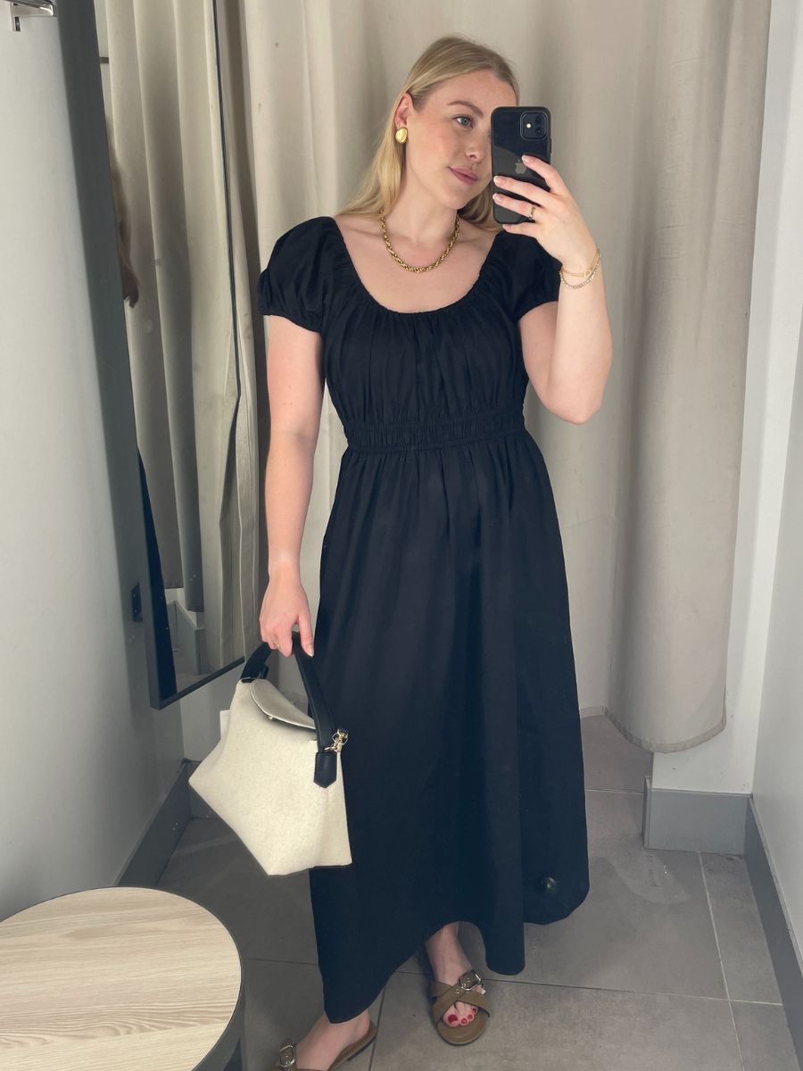 Woman wears black dress, gold jewellery, carries canvas tote bag and wears suede sandals