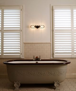vintage bathroom design with a claw foot tub and shutters at the window