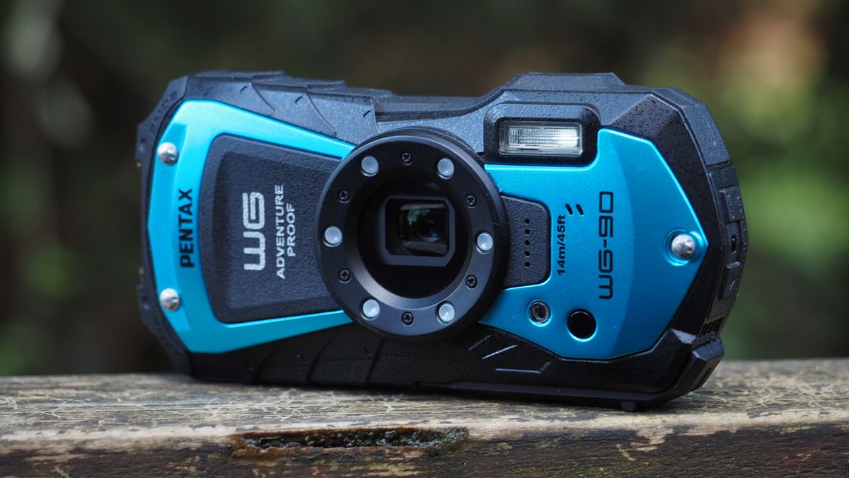 Close up of a Pentax WG-90 sitting on a wooden surface in front of woodland