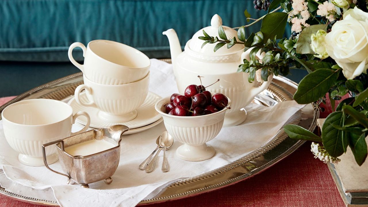 Silver tray set with white teacups, saucers and teapots and a bowl of cherries