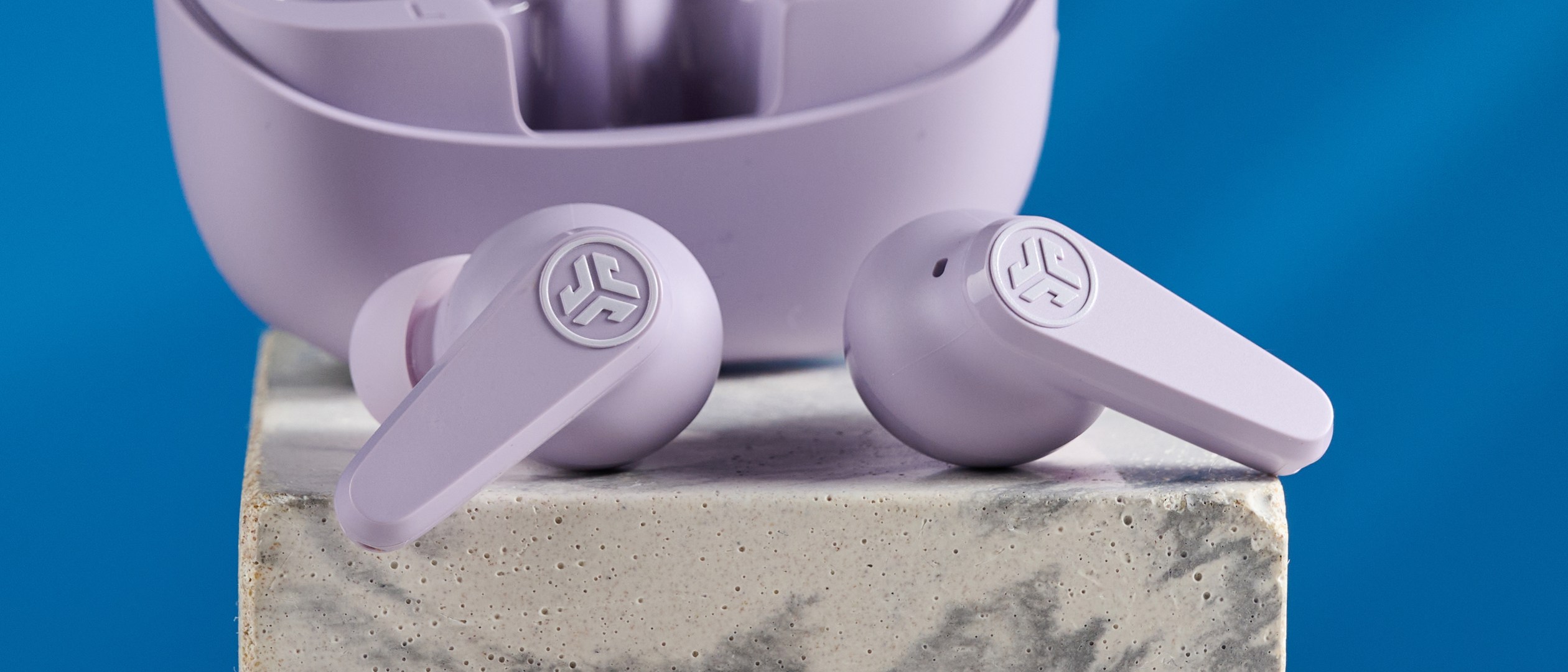 the jlab go pods anc earbuds in lilac with a lilac charging case and built in usb-c cable against a blue background on a marble stand