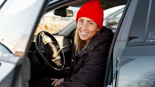 A woman wearing a red wool hat and black puffer jacket in her car