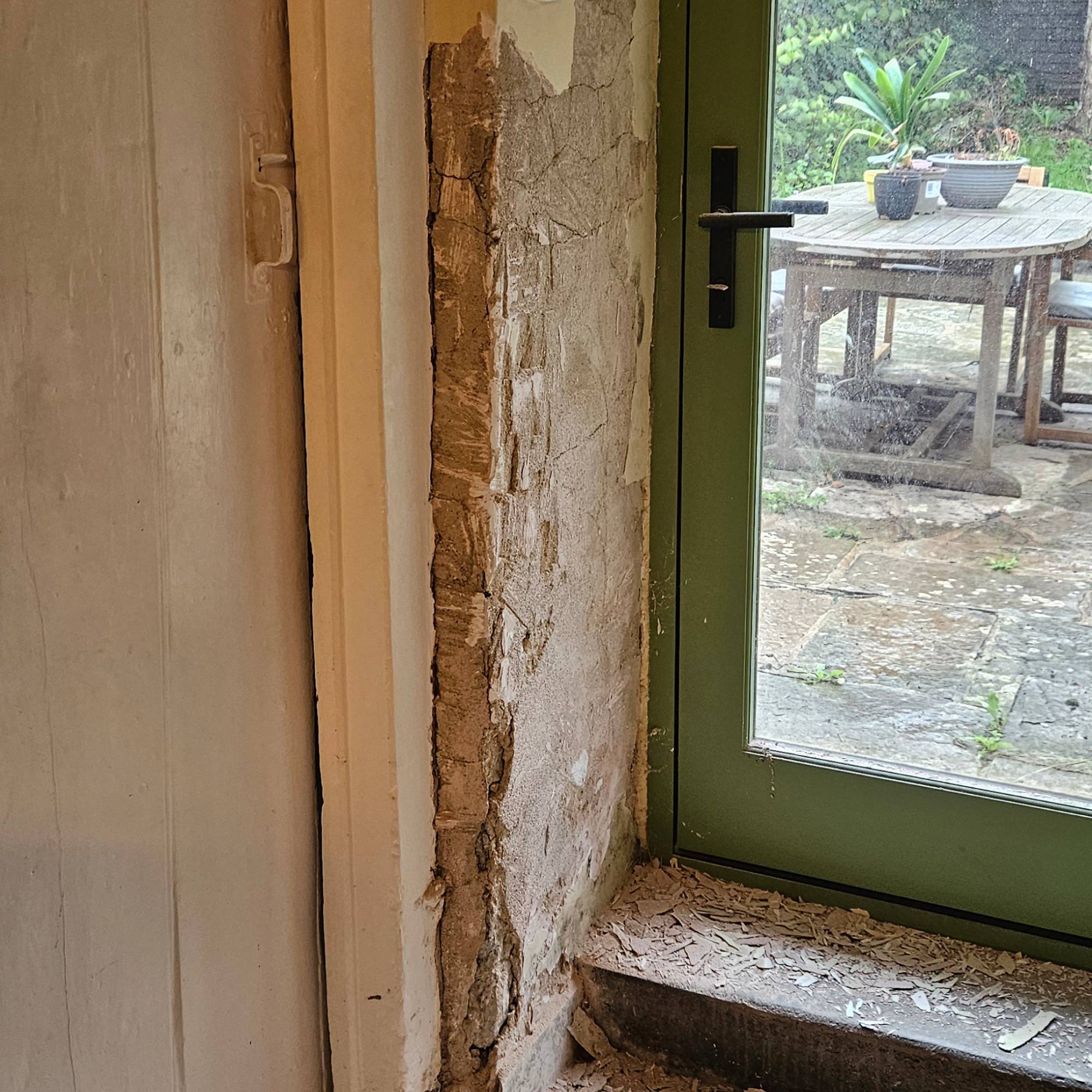 plaster being chipped off wall next to green external door and white wood door