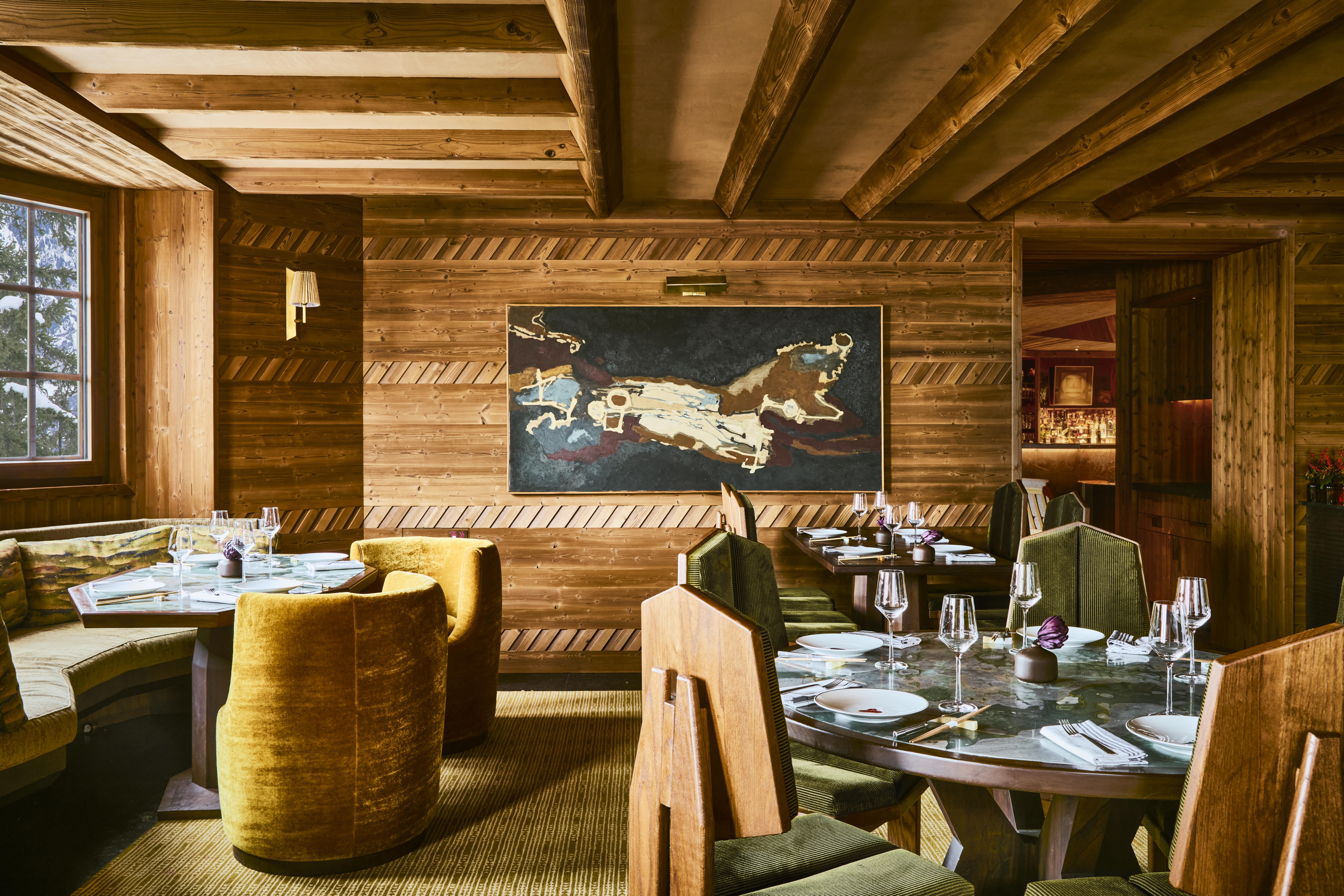 The elaborate, theatrical interiors of a ski chalet with wood wall paneling, plush textiles in different patternes, colors, and textures, plenty of paintings and sculptures adorning its halls, and a dimly lit atmosphere.