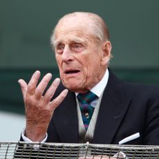 Prince Philip wears a suit with a waistcoat and tie and looks bemused while holding one hand out, he has gray hair and thinning gray hair in 2016