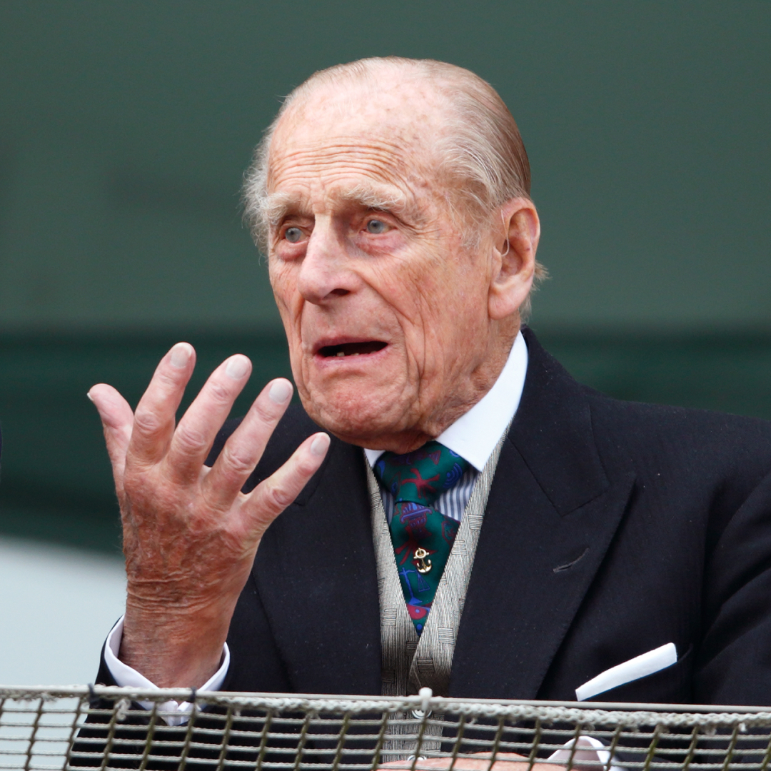 Prince Philip wears a suit with a waistcoat and tie and looks bemused while holding one hand out, he has gray hair and thinning gray hair in 2016