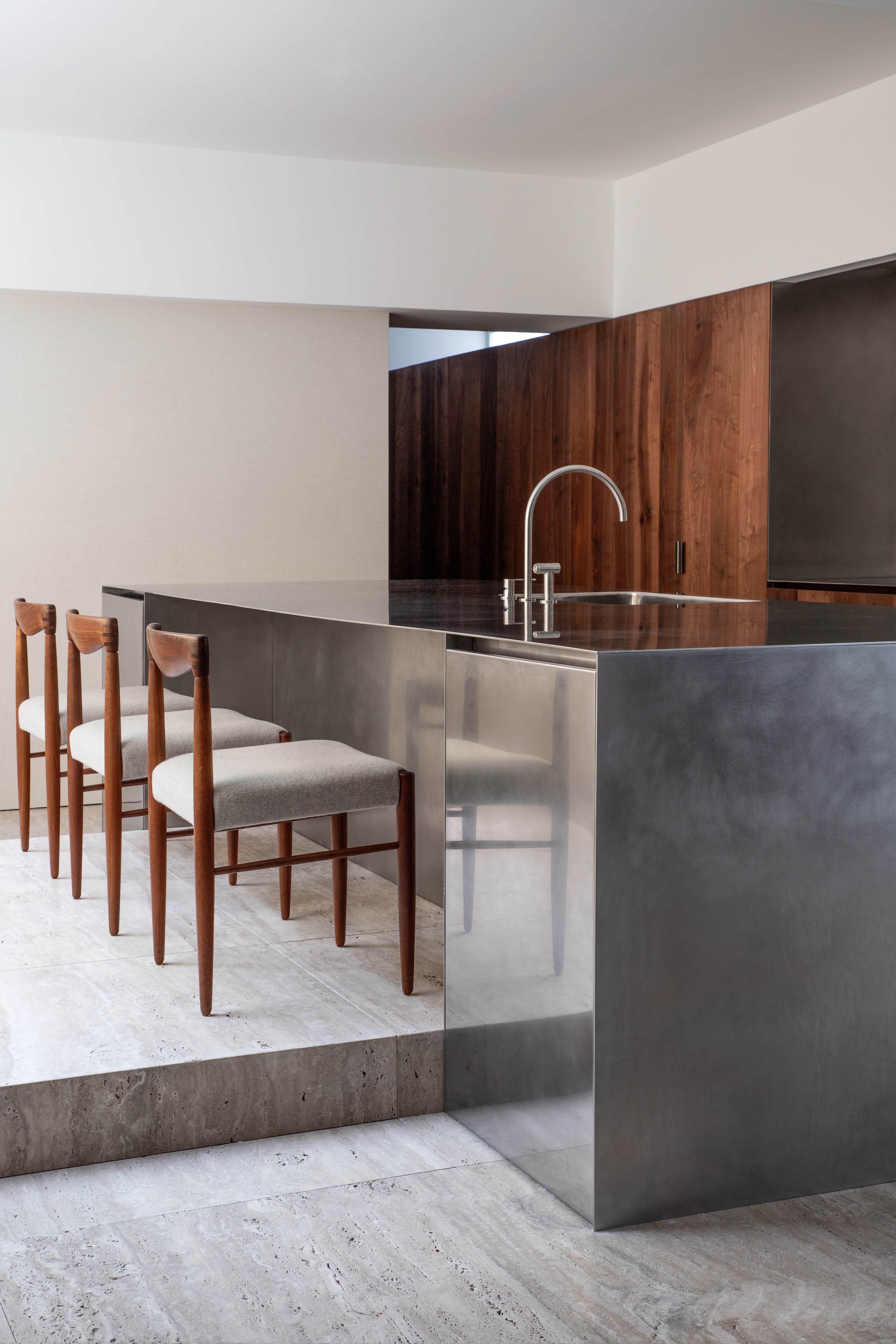 A kitchen with a fully stainless steel island and bar stools beside it